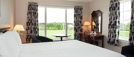 A hotel room with a large bed, two chairs, a small table, a desk with a lamp, and a mirror.