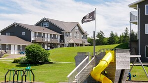 A playground with a yellow slide and swings, set against a backdrop of residential buildings and a flag. - Brackley Beach Northwinds Inn and Suites (Brackley Beach)