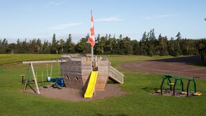 A playground with a slide, swings, and a flagpole with a flag. - Brackley Beach Northwinds Inn and Suites (Brackley Beach)
