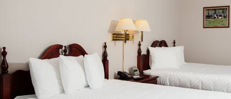 A hotel room with two beds, a nightstand with a phone and remote controls, and a wall-mounted lamp.
