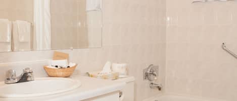 A bathroom with a vanity, sink, mirror, and a bathtub.