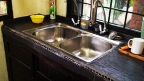A kitchen with a double stainless steel sink, a yellow bowl, a can of soda, and a white mug on the counter. - Step Inn Guest House (Kuala Lumpur)