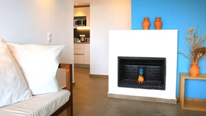 A living room with a white sofa, a fireplace, and a kitchen in the background. - Mika Villas & Suites (Hersonissos)