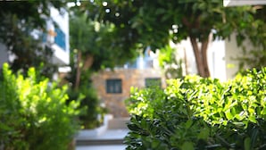 A narrow pathway flanked by lush greenery and a stone building with a window. - Mika Villas & Suites (Hersonissos)
