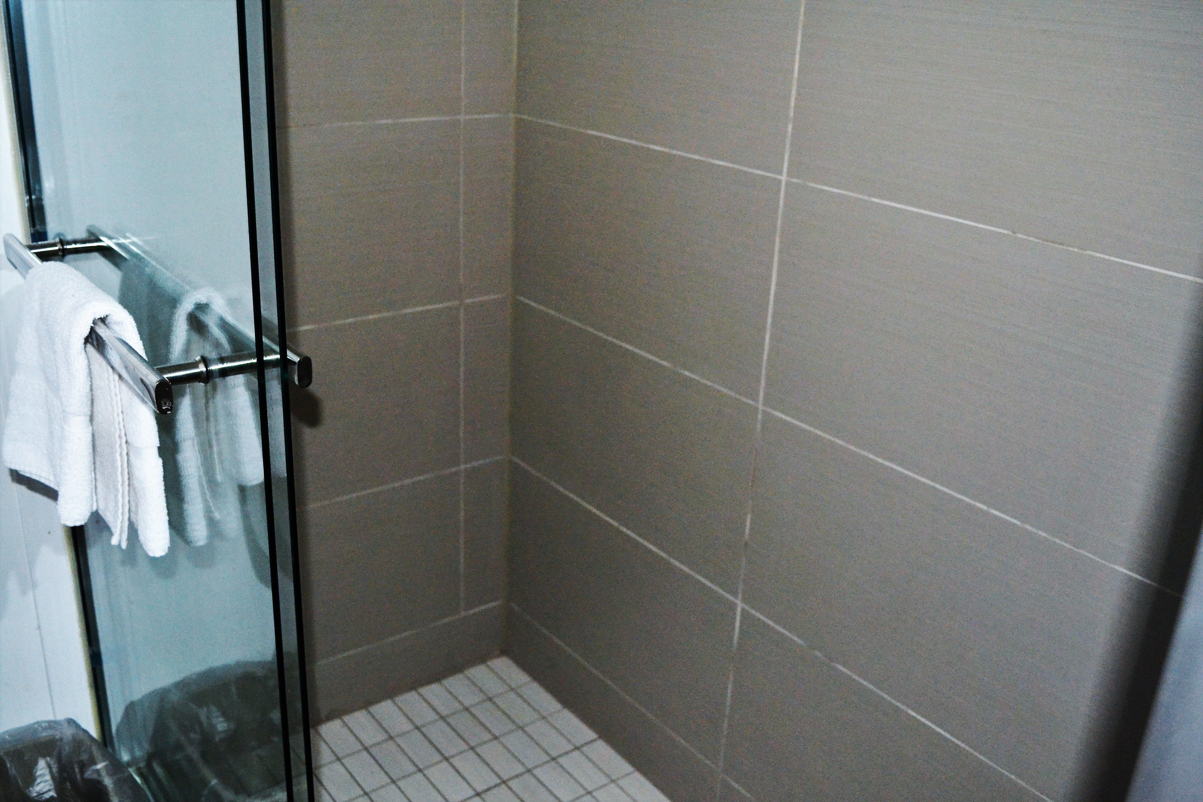 A shower with a glass door, tiled walls, and a metal towel rack with white towels.
