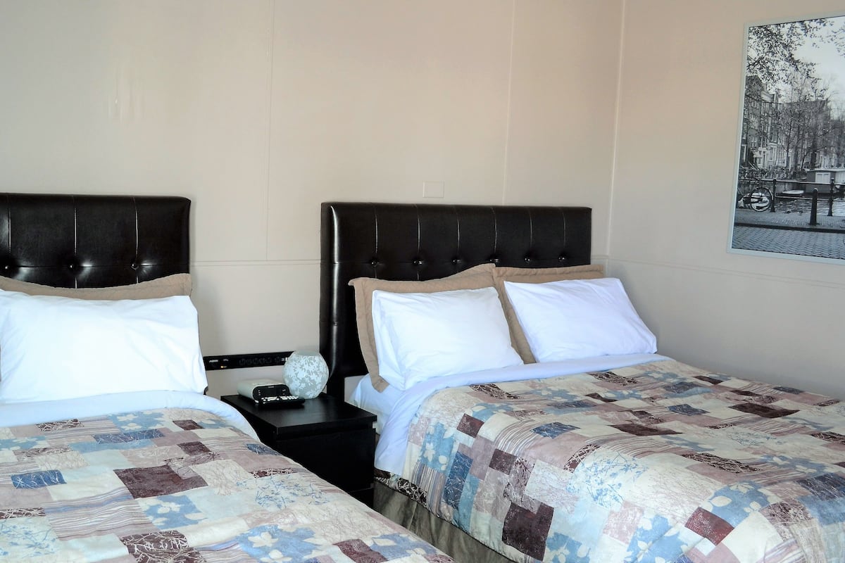 Two beds with headboards, a nightstand with a lamp, and a wall-mounted picture.