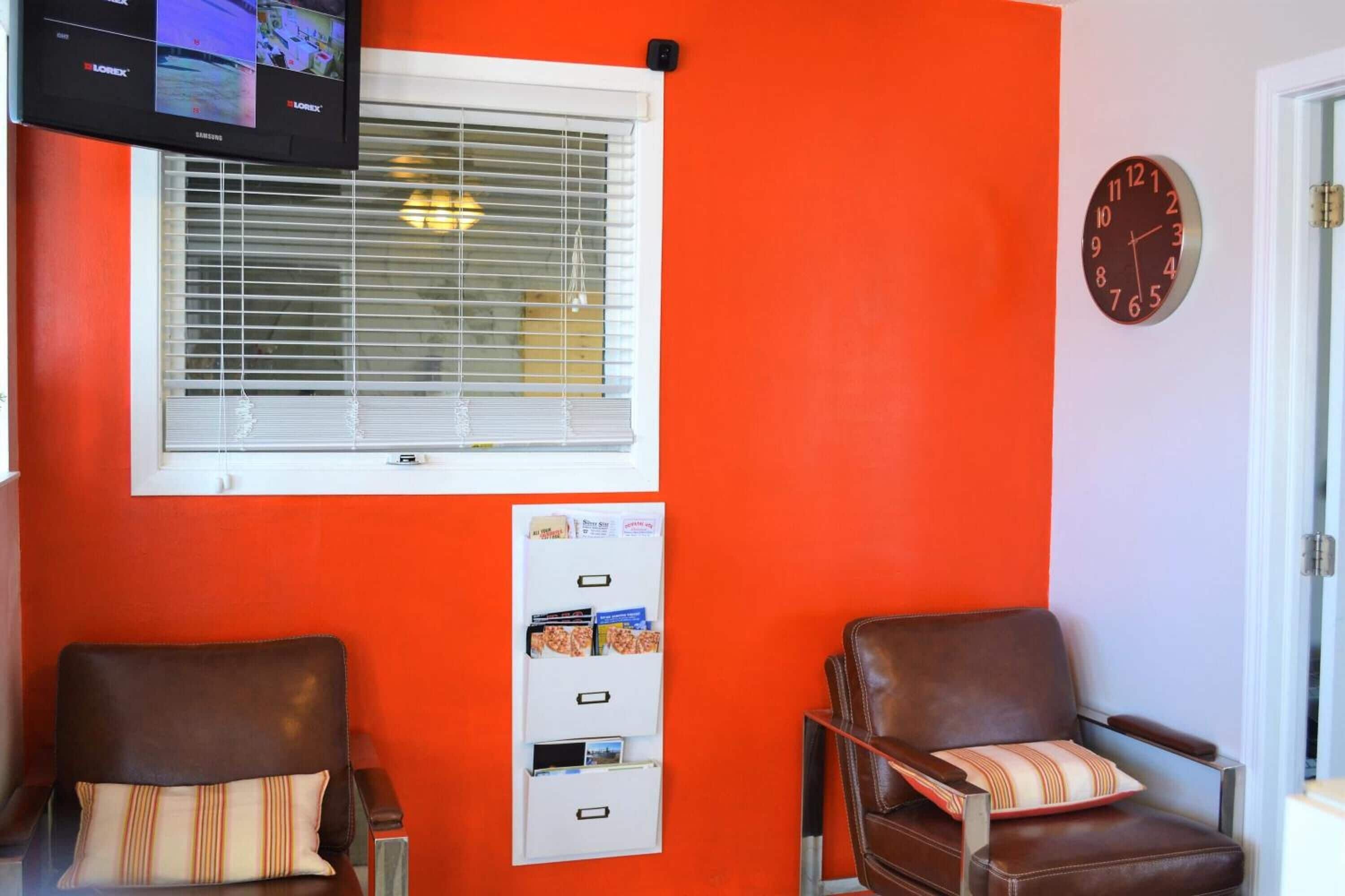 Una habitación con dos sillones de cuero, un reloj de pared, un televisor instalado y una ventana con persianas.