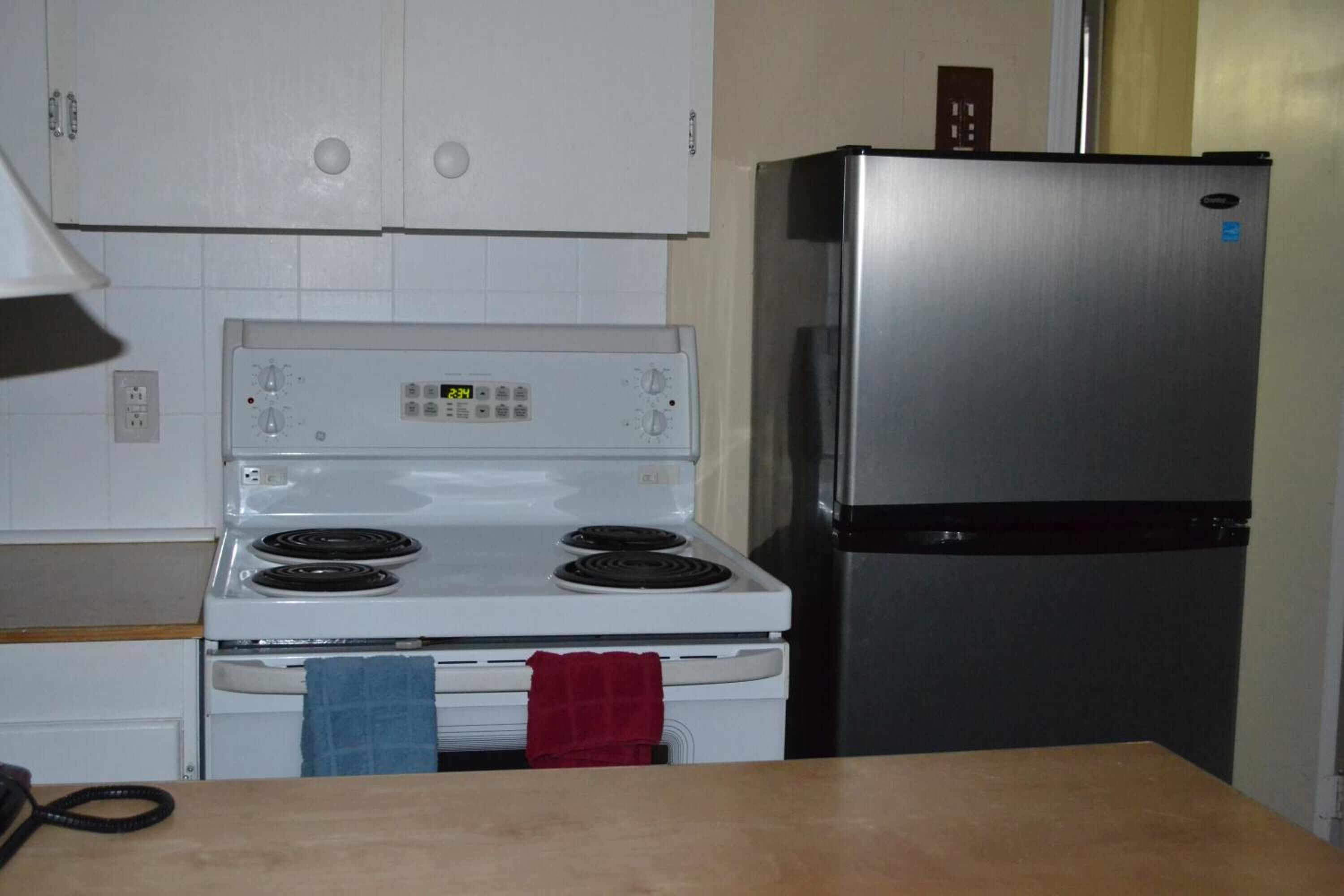 A kitchen with a white stove, a stainless steel refrigerator, and white cabinets.