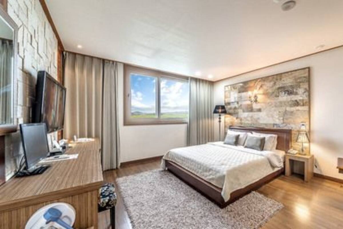Habitación de hotel moderna con una cama grande, un escritorio con computadora, un televisor y vistas al exterior.
