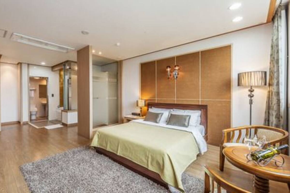 Una habitación de hotel moderna con una cama grande, una mesita de noche, una silla y una pequeña mesa con una botella.