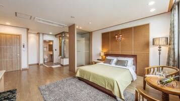 A modern hotel room with a large bed, a bedside table, a chair, and a small table with a bottle.