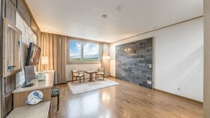 Una sala de estar moderna con piso de madera, pared de acento de piedra, comedor con mesa y sillas, y un ventanal con vista al exterior.