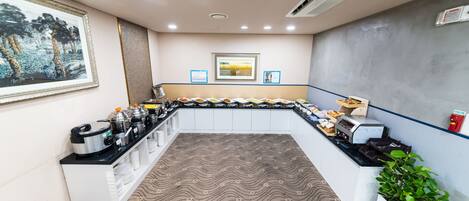 A hotel kitchen with a buffet setup, including food containers and a coffee machine.