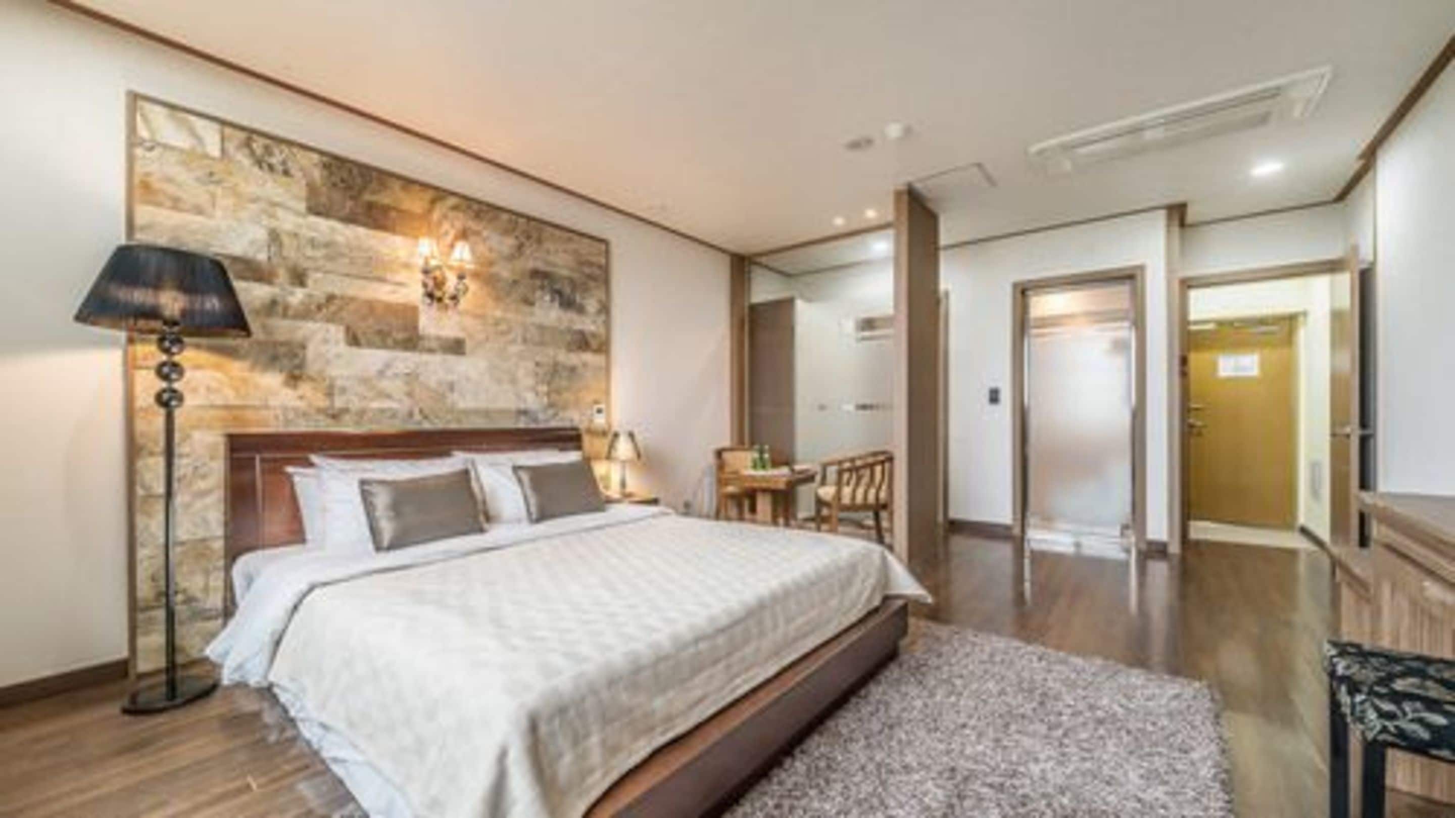 A hotel room with a large bed, a stone accent wall, a desk, and a chair.