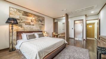 A hotel room with a large bed, a stone accent wall, a desk, and a chair.