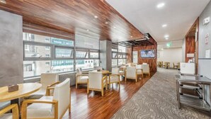 Un moderno vestíbulo de hotel con paneles de madera, ventanas amplias y un televisor de pantalla plana en la pared.