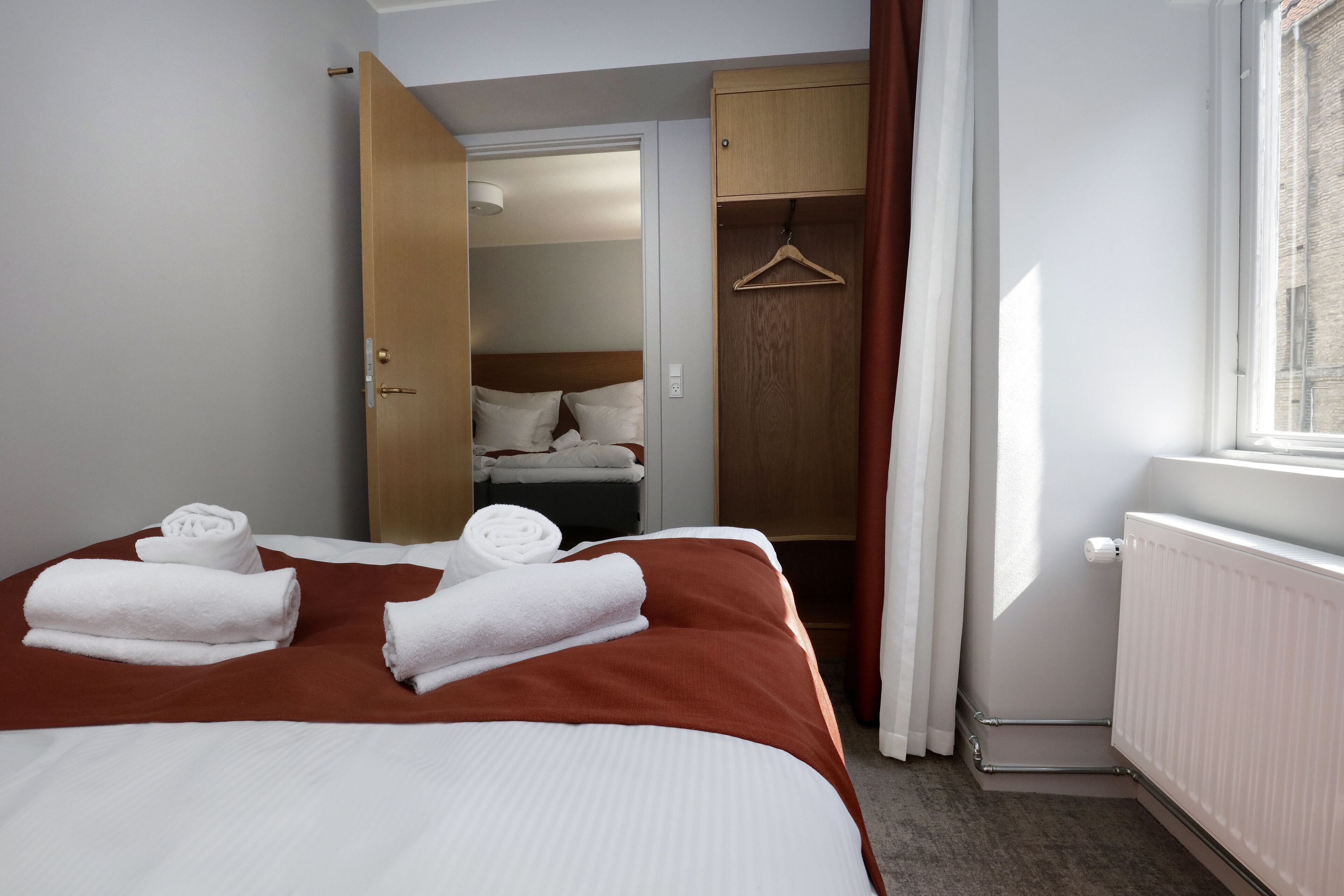 Ein Hotelzimmer mit einem Bett, einem Holzschrank, einem Kleiderhaken und einem Fenster mit Vorhängen.