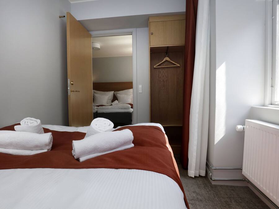 Una habitación de hotel con cama, armario de madera, perchero y ventana con cortinas.