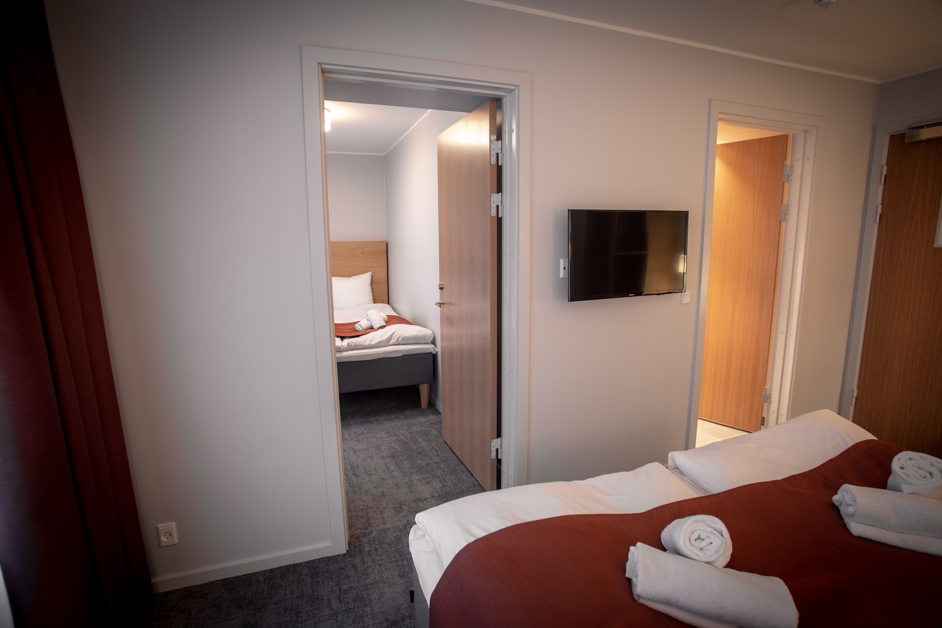 A hotel room with a bed, a TV, and a door leading to another room.