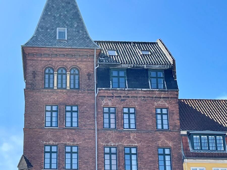 Un edificio de ladrillo de varios pisos con una torre destacada y ventanas de arco.