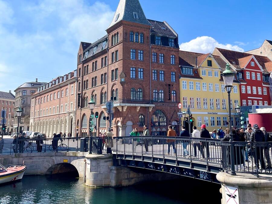 A historic building with a prominent tower, a bridge with pedestrians, and a canal with a boat.