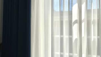 A window with sheer white curtains and a dark blue curtain partially drawn.
