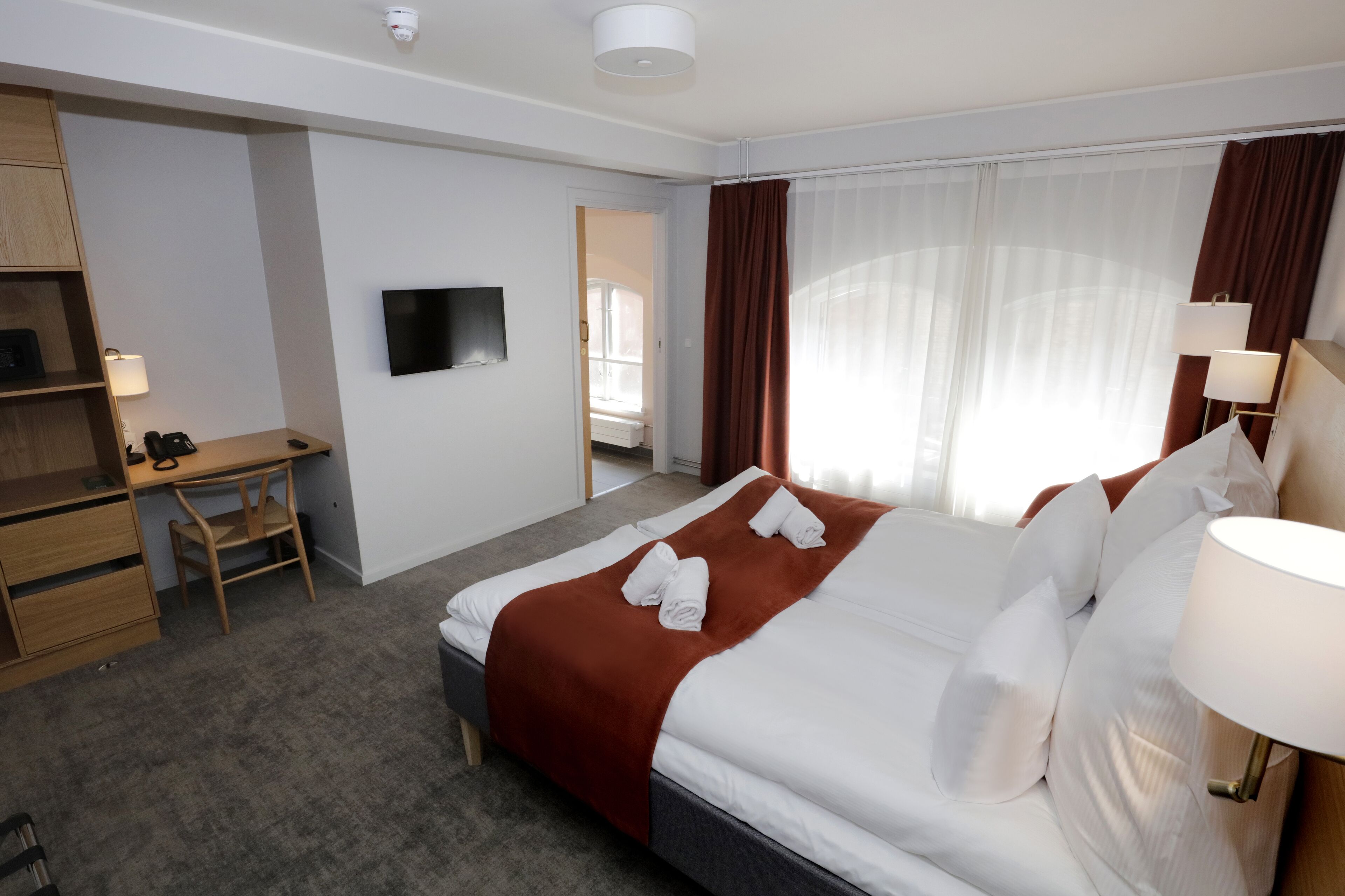 A hotel room with a bed, a desk, a TV, and a window with curtains.