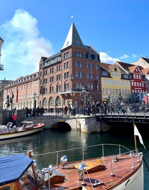 En historisk byggnad med ett markant torn, en bro där fotgängare kan gå, och båtar som ligger förtöjda i en kanal.
