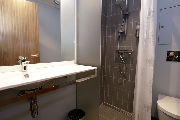 A bathroom with a wooden door, a white sink, a shower with a glass door, and a toilet.