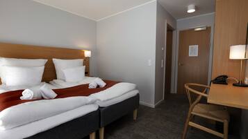 Quarto de hotel com uma cama, duas mesas de cabeceira, uma escrivaninha e uma cadeira, além de uma porta.