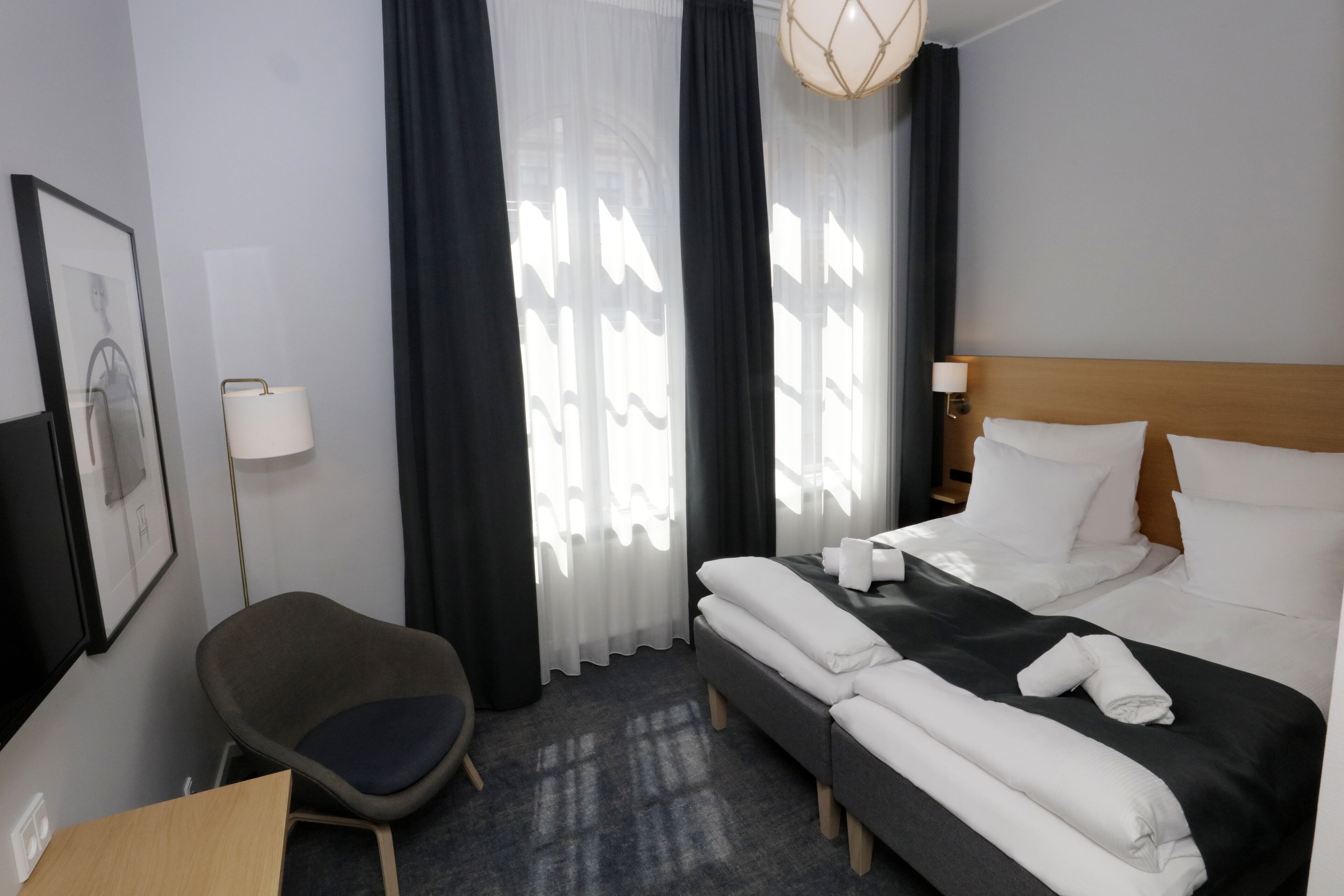 A hotel room with a bed, a chair, a desk, and a window with curtains.