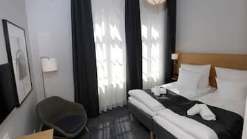 Una habitación de hotel con cama, una silla, un escritorio y una ventana con cortinas.