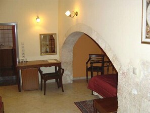 A room with a desk, a chair, a bed, and an arched doorway. - Belmondo Hotel (Chania)
