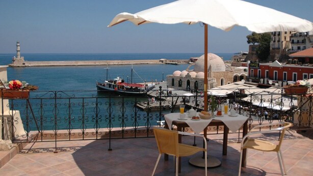 Una terraza con mesa y sillas, con vista a un puerto con barcos y un faro.