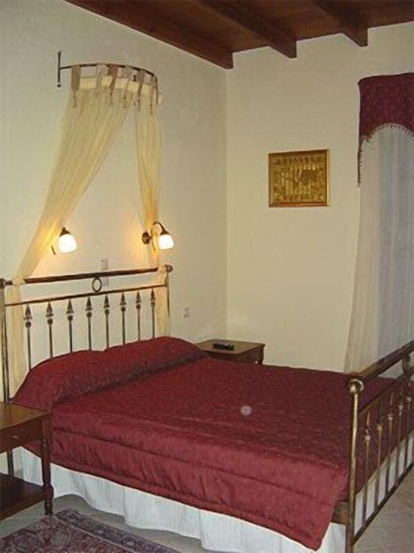 A bedroom with a wooden bed frame, a red bedspread, a nightstand, a lamp, and a painting on the wall.