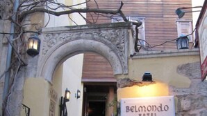 Entrada de un hotel con un cartel que dice "Belmondo Hotel", un arco de piedra y una pequeña chimenea.