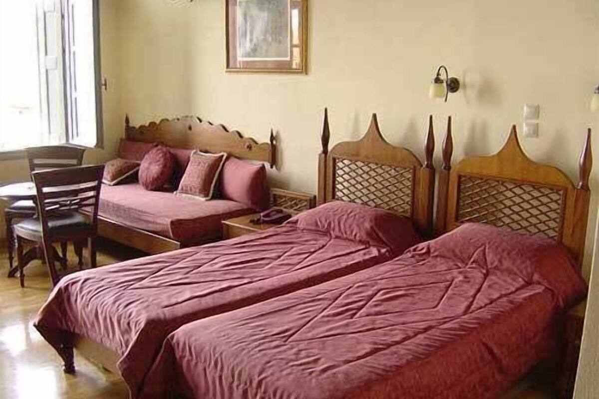 Un dormitorio con dos camas individuales, cabecera de madera, mesita de noche, una silla y un cuadro en la pared.