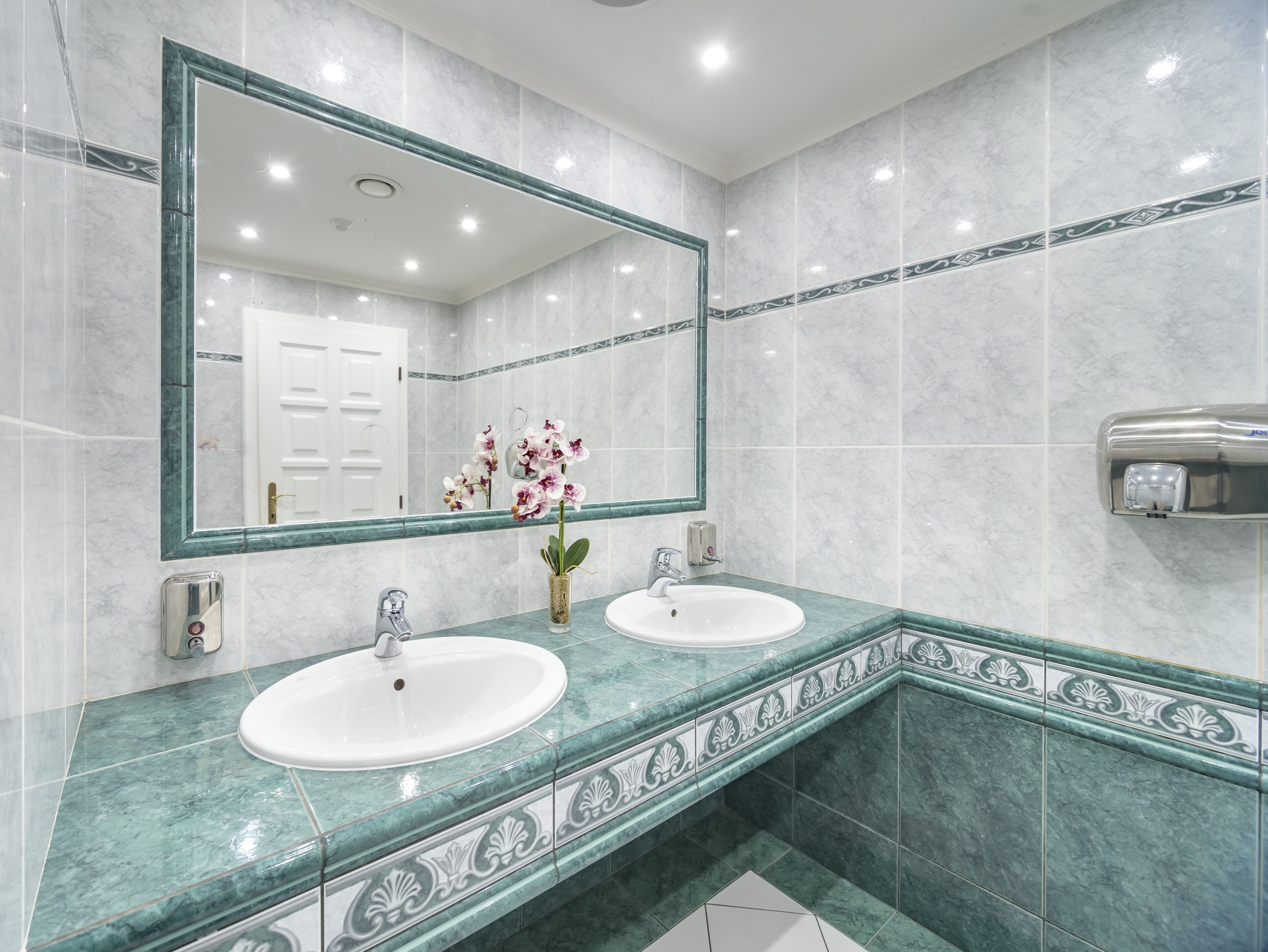 A bathroom with two sinks, a large mirror, and a hand dryer.