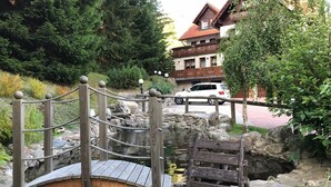 A wooden bridge over a pond with a stone wall and a wooden bench. - Hotel Kristýna (Spindleruv Mlyn)