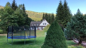 A house named Kristjana with a trampoline in the yard, surrounded by trees and a mountain in the background. - Hotel Kristýna (Spindleruv Mlyn)