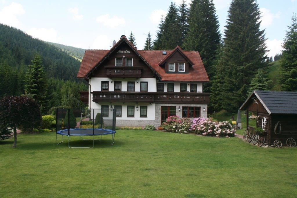 A two-story building with a red-tiled roof, surrounded by lush greenery and trees.
