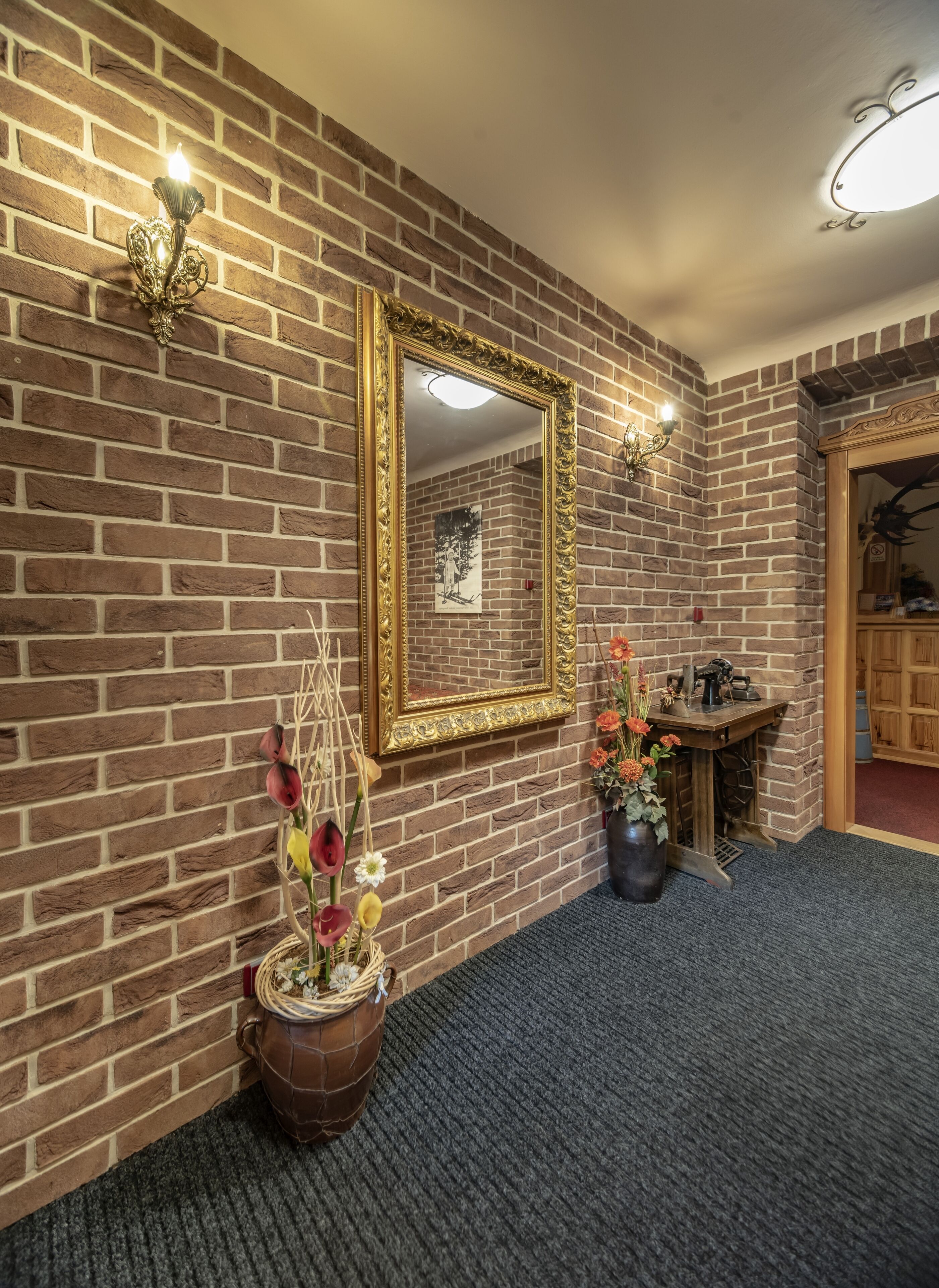 A room with a brick wall, a large mirror, a vase with flowers, and a wooden cabinet.