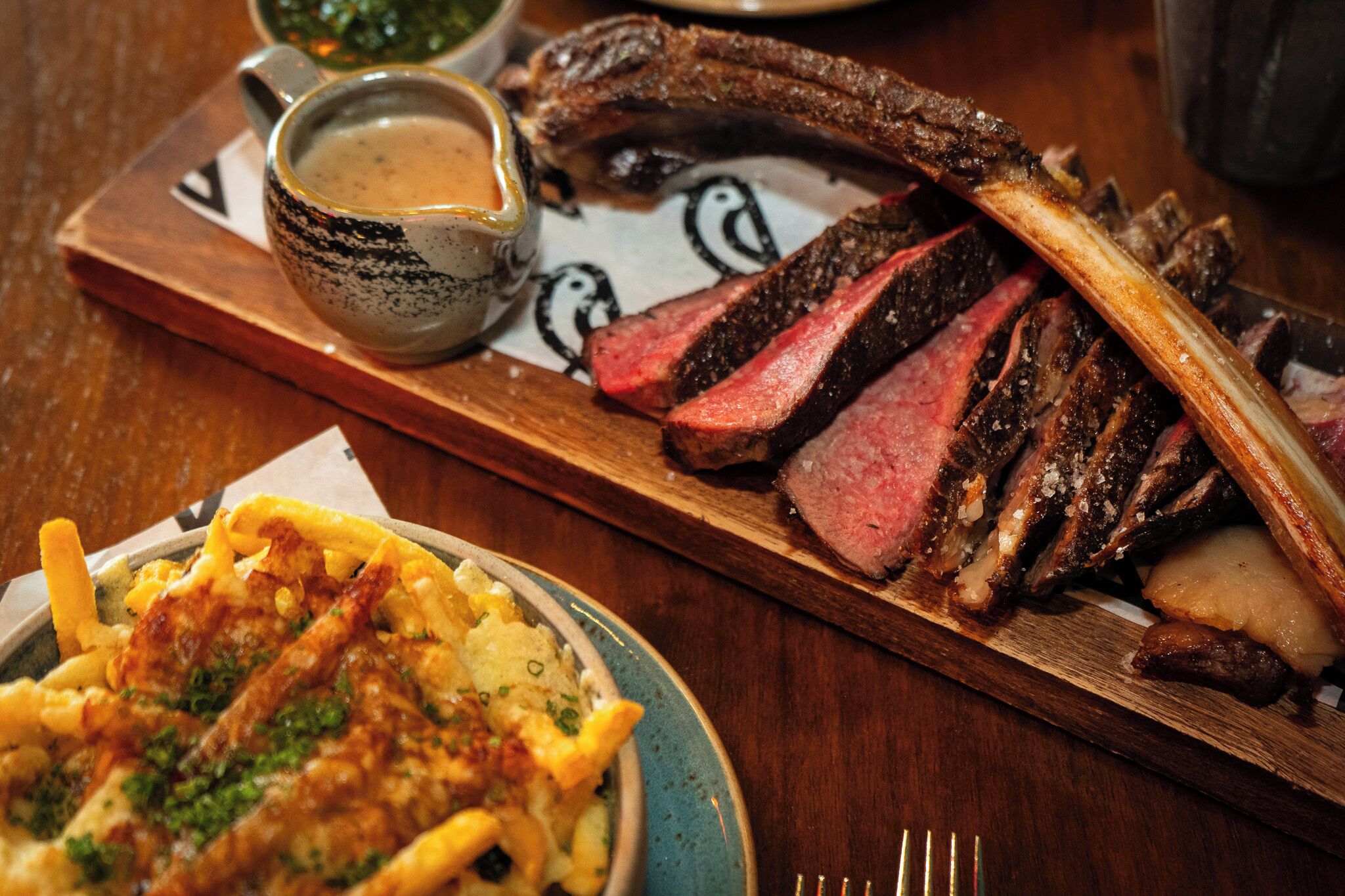 A steak with fries and a cup of sauce on a wooden board.