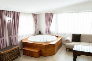 A modern bathroom with a freestanding bathtub, a wooden bench, a sofa, and a coffee table. - Infinity City Hotel (Fethiye)