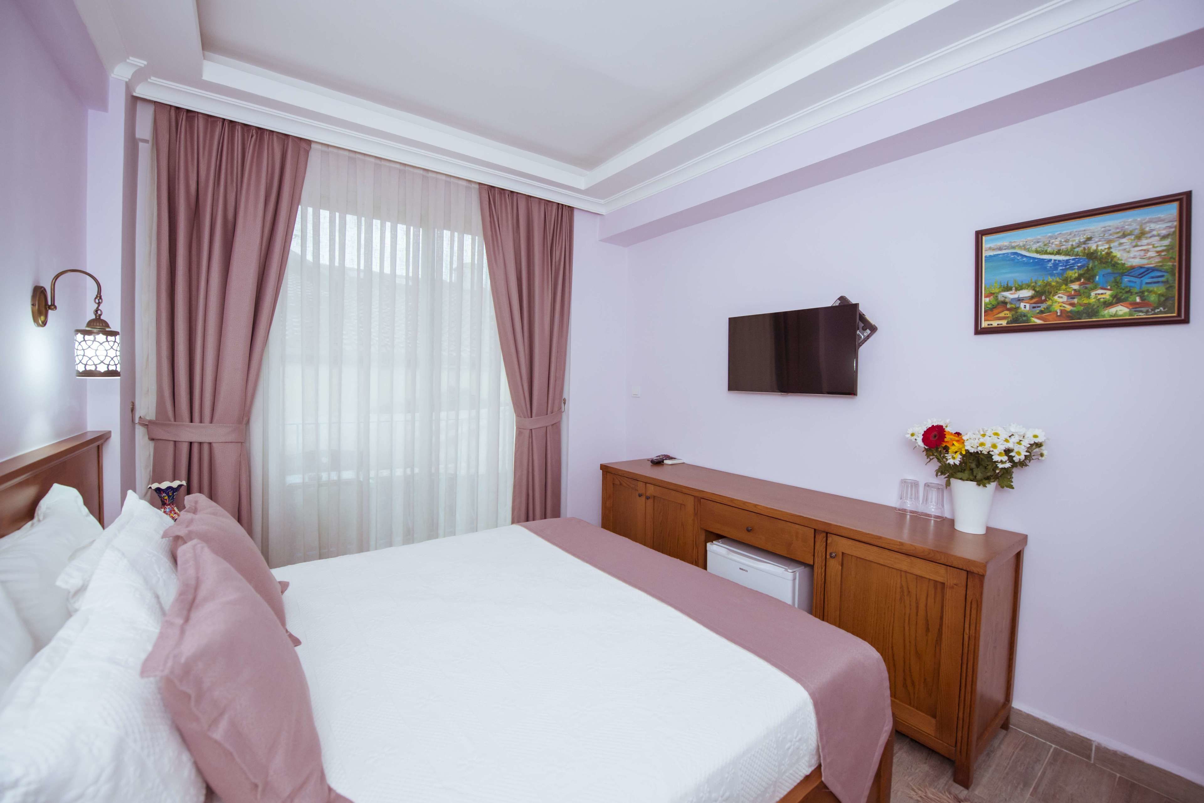 A hotel room with a bed, a wooden desk, a television, and a painting on the wall.