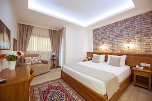 Hotelkamer met een groot bed, een houten hoofdbord, een accentmuur van baksteen, een kleine tafel met een bloemenvaas en een bank met een patroonkleed.