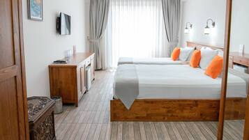 A hotel room with a wooden bed frame, two beds with white and orange pillows, a wooden dresser, a television, and a window with curtains.