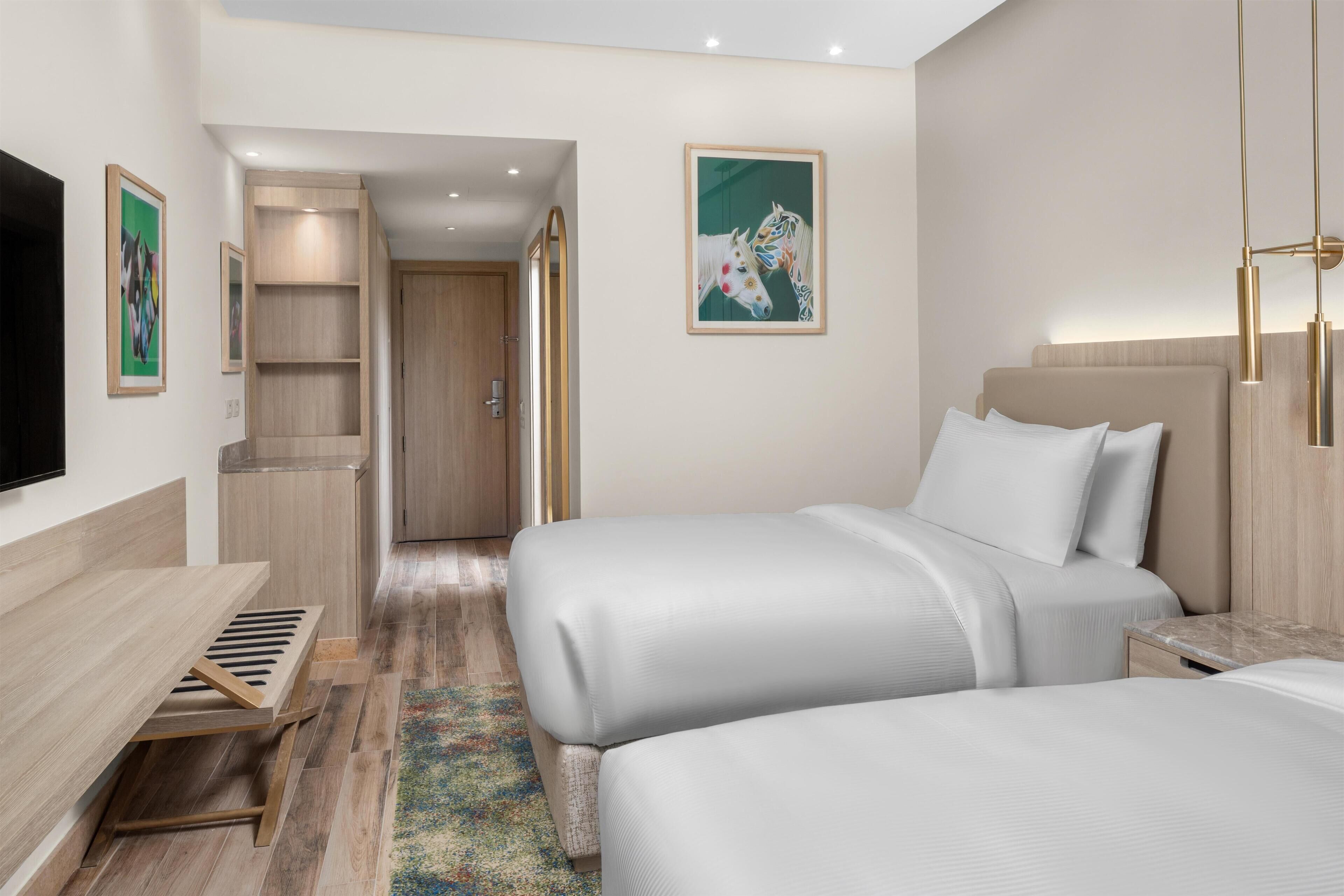 Una habitación de hotel con dos camas, televisor, escritorio y estantería.