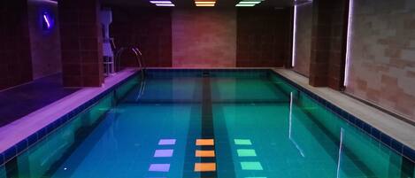 Una piscina interior con suelo de baldosas y techo con paneles de luz rectangulares.