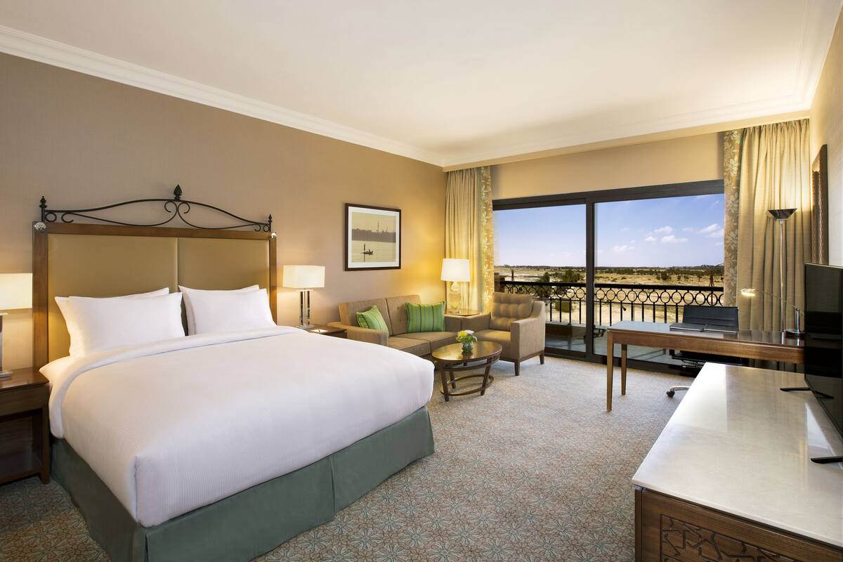 Une chambre d’hôtel avec un grand lit, un bureau, une chaise, un canapé et un balcon avec vue.